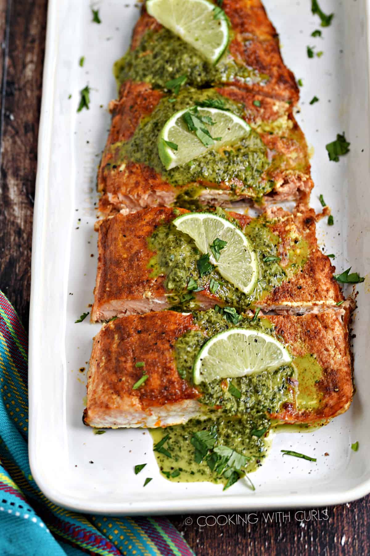 Baked salmon filet topped with cilantro lime sauce on a white platter.