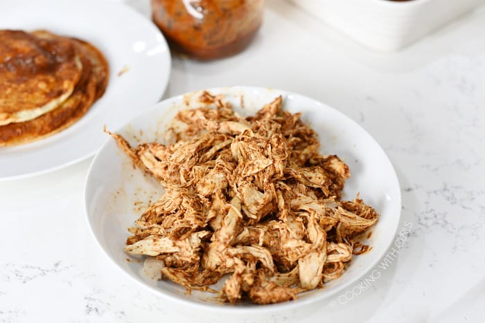 Shredded chicken mixed with enchilada sauce in a bowl.