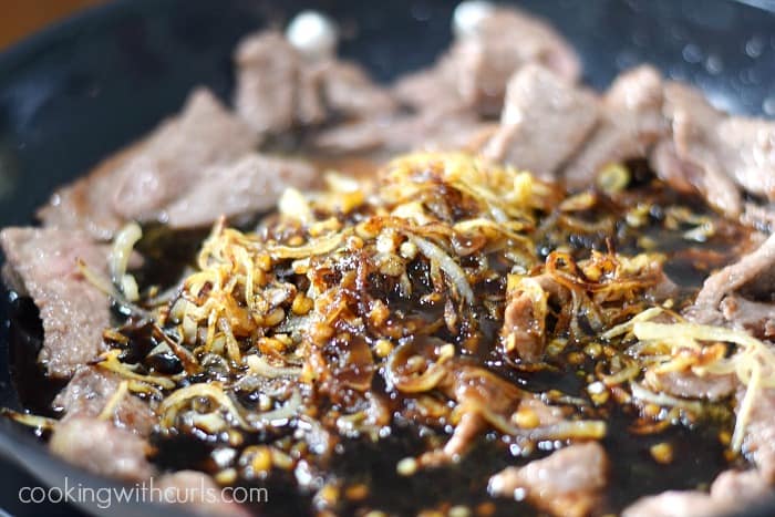 Strips of beef with sauce and caramelized onions in a skillet.