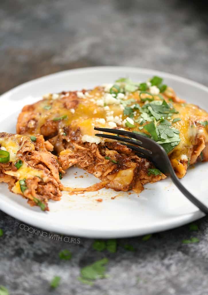 A chicken enchilada cut with a black fork on a white plate.