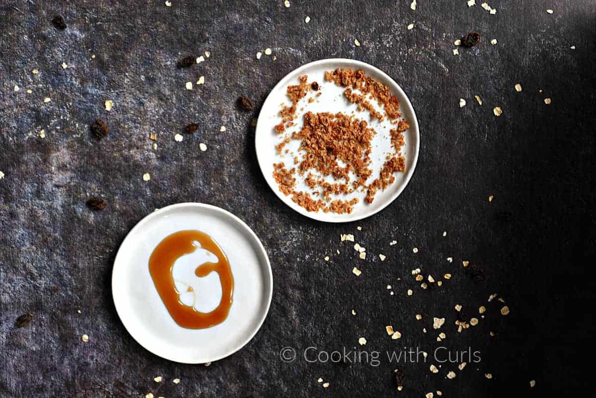 Oatmeal cookie crumbs on a small plate next to honey on a small plate. 