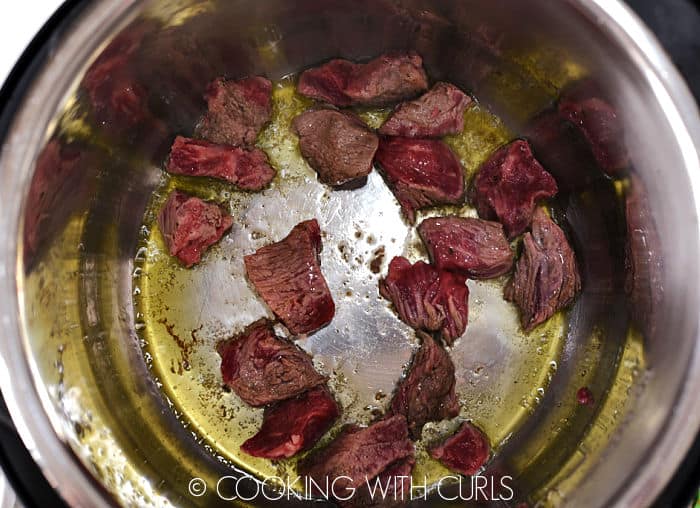 Oil and beef chunks sizzling in a pressure cooker. 