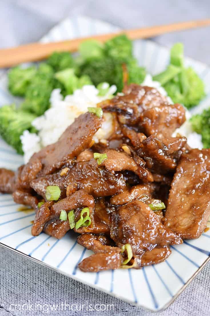 Sauce covered strips of beef on a plate with steamed rice and broccoli.