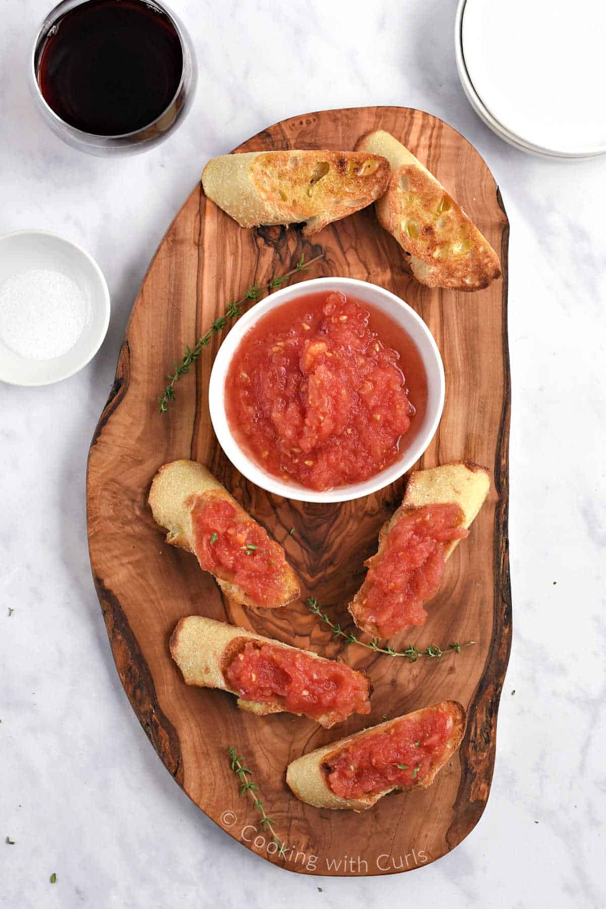 Pan con tomate toasts on a wood board surrounding a bowl of grated fresh tomatoes.