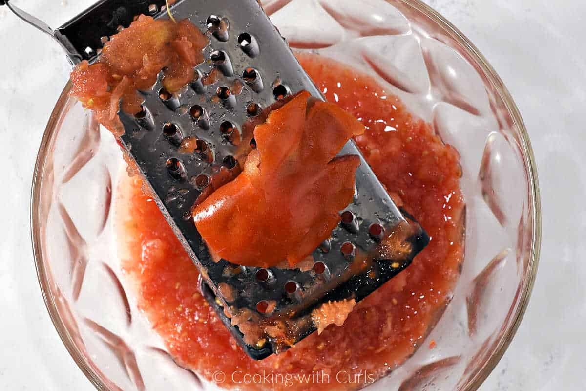 Box grater in a large bowl with grated fresh tomatoes.