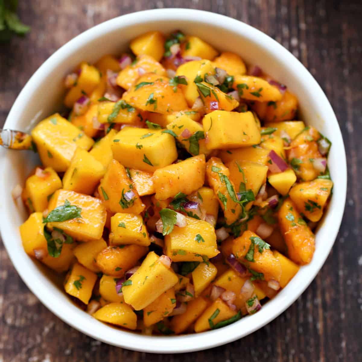 A small white bowl filled with chopped papaya, mango, red onion, cilantro, chipotle chili powder, and lime juice.