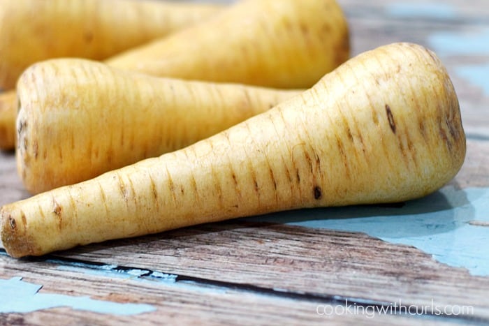 Four parsnips laying on a weathered blue surface.