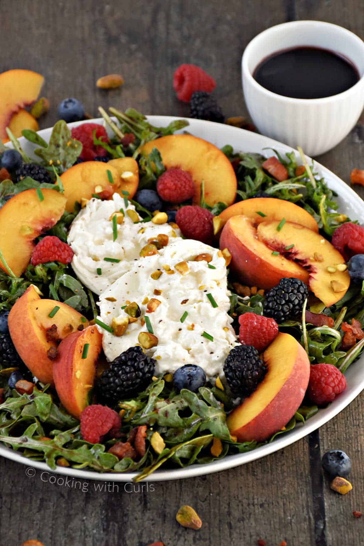 Sliced peaches, fresh berries, and fresh burrata on a bed of arugula.