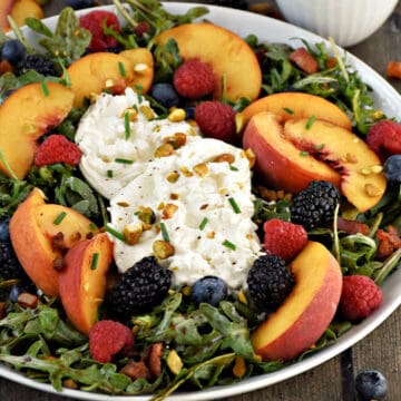 Sliced peaches, fresh berries, and fresh burrata on a bed of arugula.