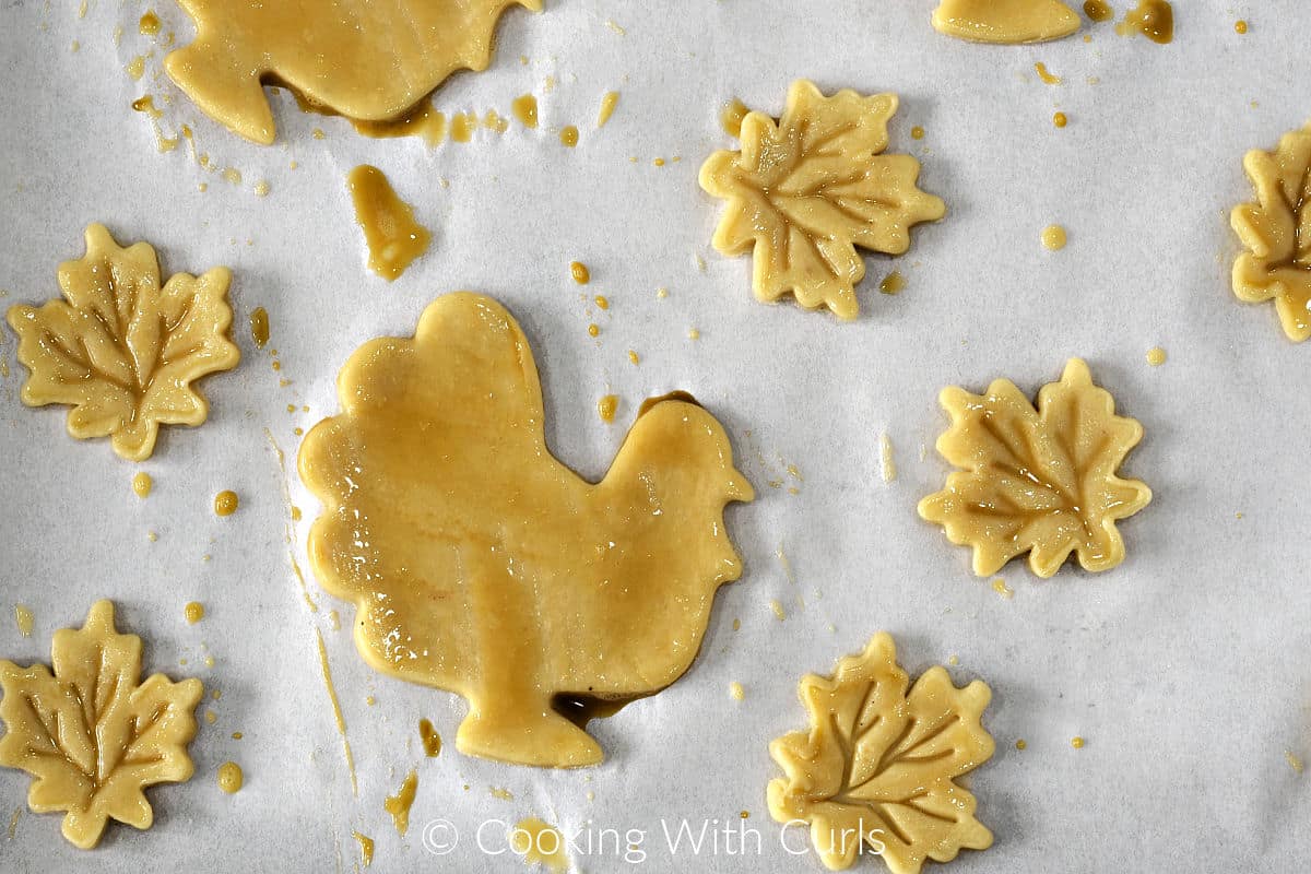 Pie crust dough cut into turkey and maple leaf shapes and brushed with egg wash on a parchment paper. 