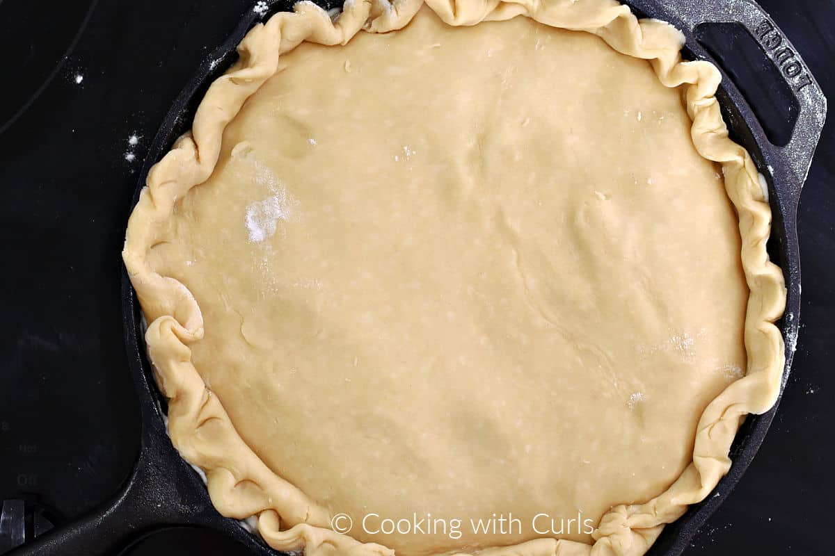 Pie crust with crimped edges over pot pie filling in a cast iron skillet. 