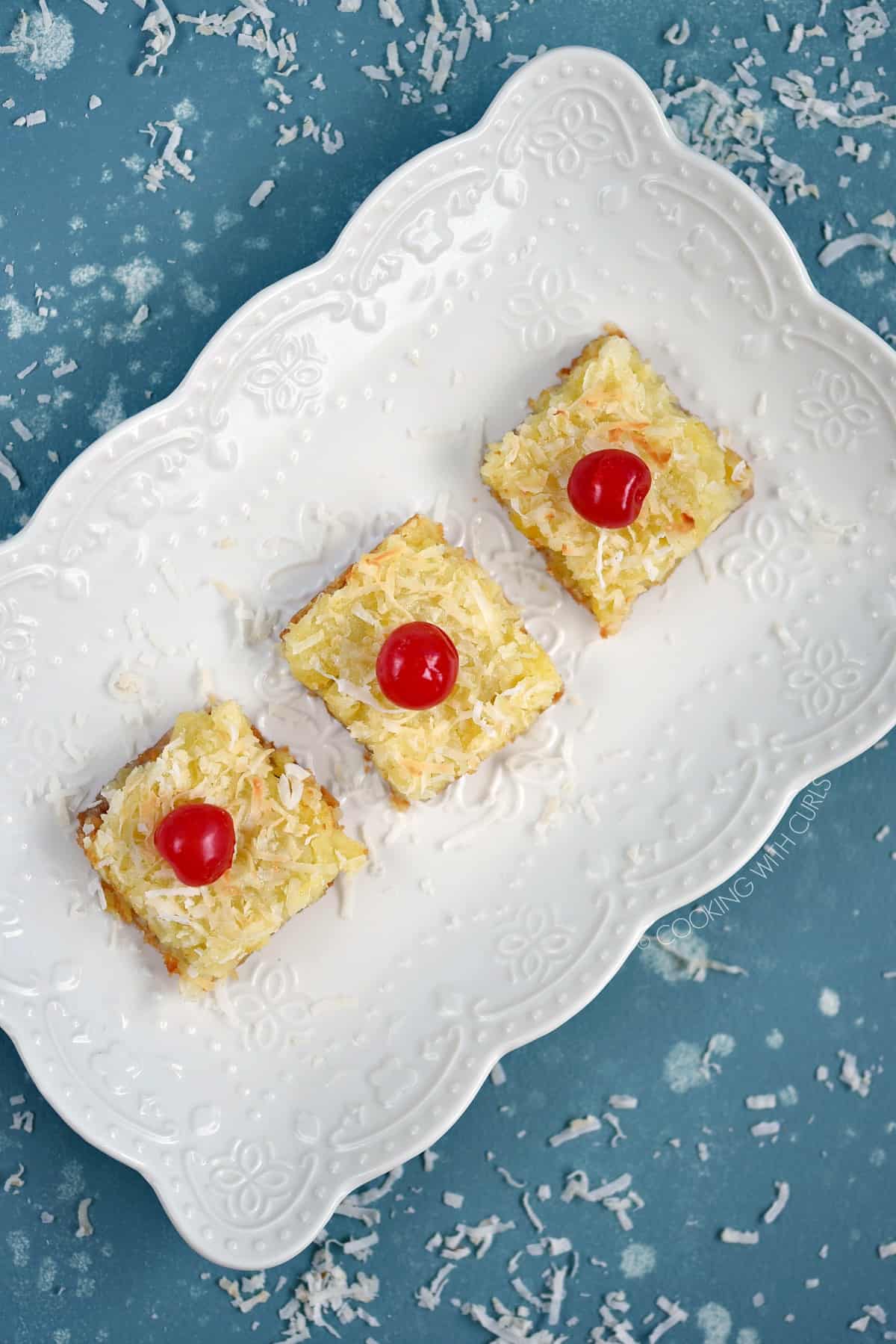 Looking down on three cherry topped Pina Colada Bars lined up on a white serving platter.