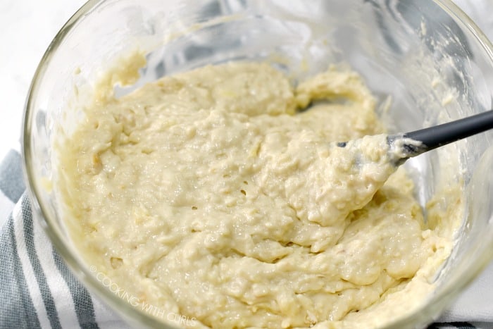 Pina Colada Muffins batter stirred together with a gray spatula in a large glass bowl.