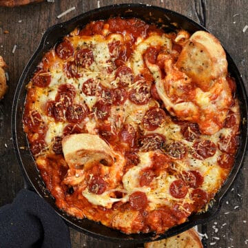 Lookin down on melty cheese, mini pepperoni, pizza dip in a cast iron skillet with toasted baguette slices.