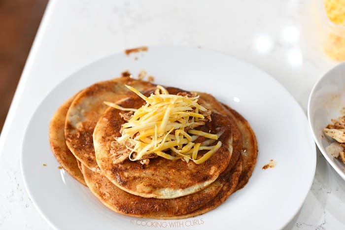 Shredded chicken and grated cheese in the center of a sauce covered tortilla.