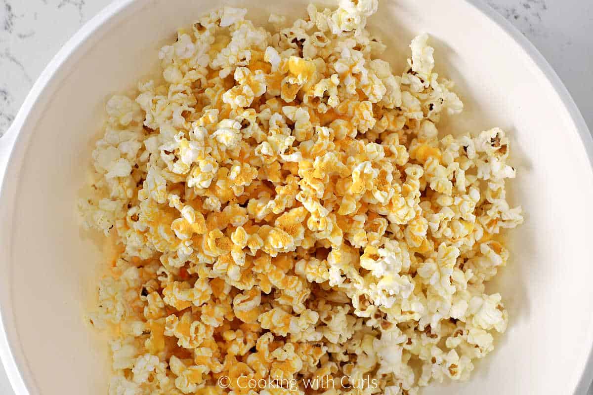 Popped popcorn in a large bowl with cheddar cheese powder sprinkled on top.