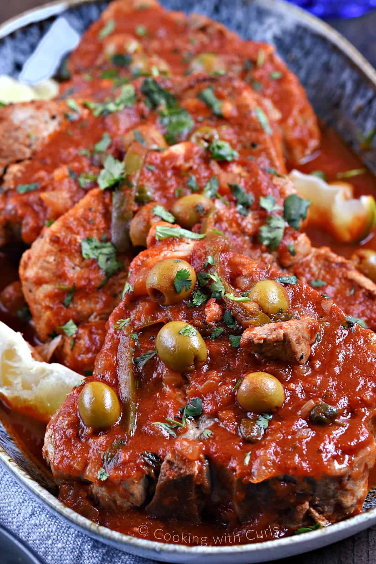 Pork chops on a platter topped with a tomato, olive, caper, and pepper sauce.