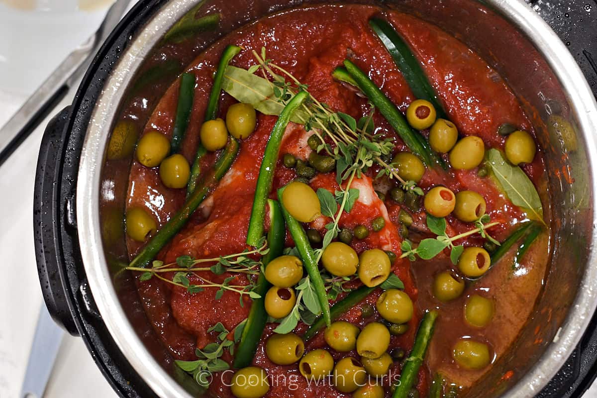 Pork chops, tomatoes, olives, herbs, and green pepper slices in a pressure cooker. 