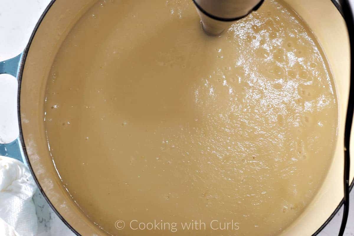Potato soup pureed with an immersion blender inside a Dutch oven. 