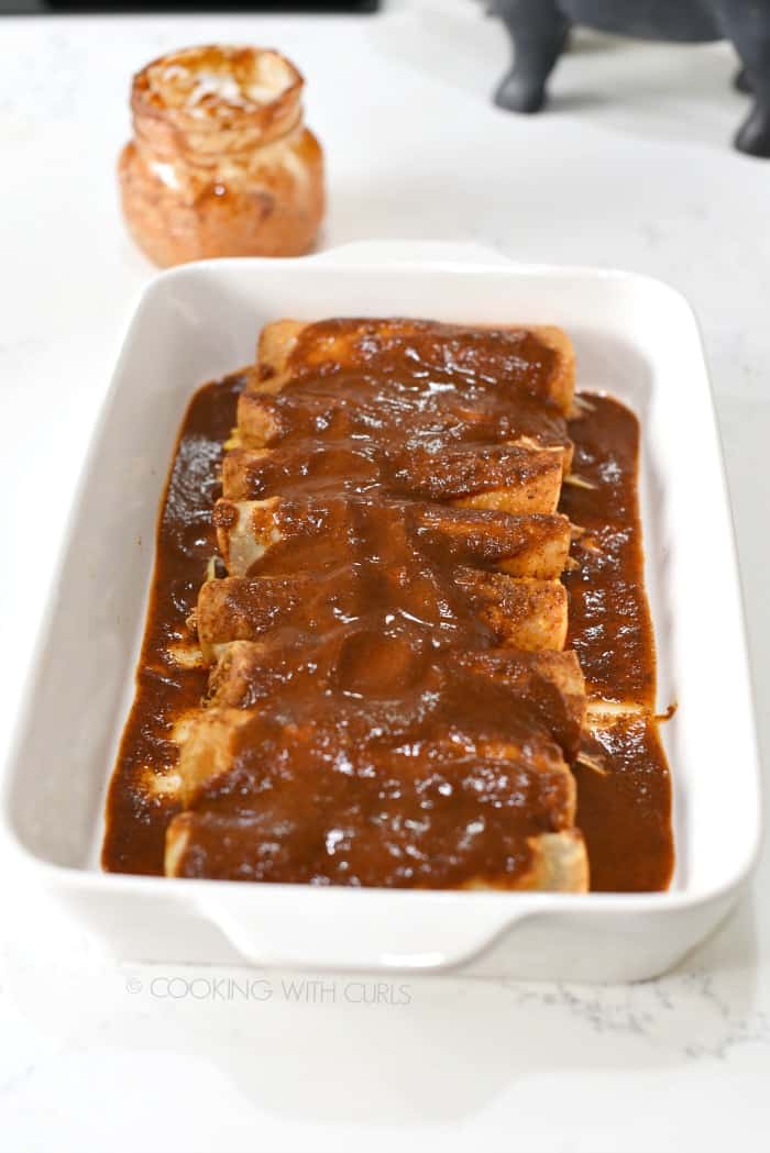 Rolled up enchiladas lined up in a baking dish and topped with extra sauce.