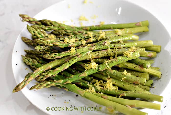 Raw asparagus tossed with oil, lemon zest and pepper in a white bowl. 