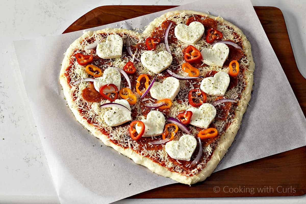 Raw heart shaped pizza on parchment paper lined pizza peel.