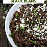 Refried Black Beans in a serving bowl topped with crumbled cheese and cilantro with title graphic across the top.