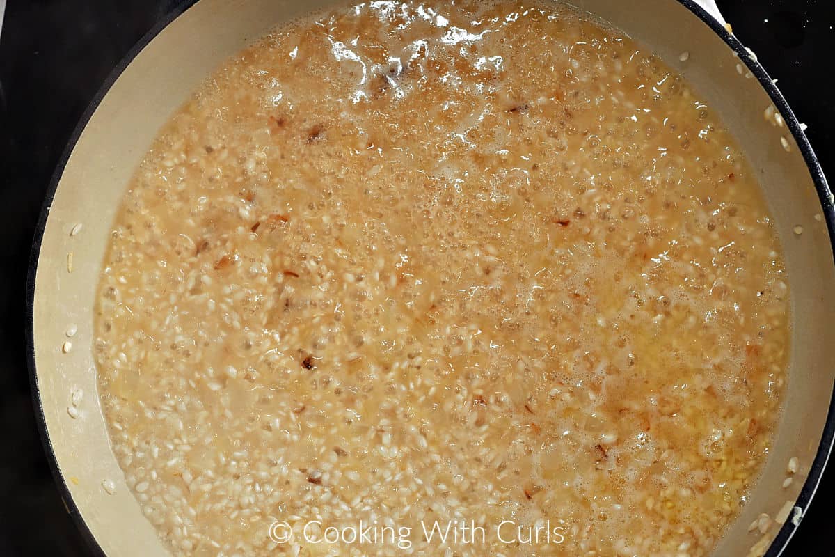 Rice mixture simmering in white wine in a large skillet. 