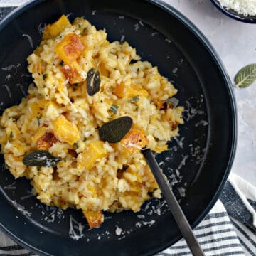 Looking down on a blue bowl with risotto, cubes of roasted butternut squash, crispy sage leaves and grate parmesan.