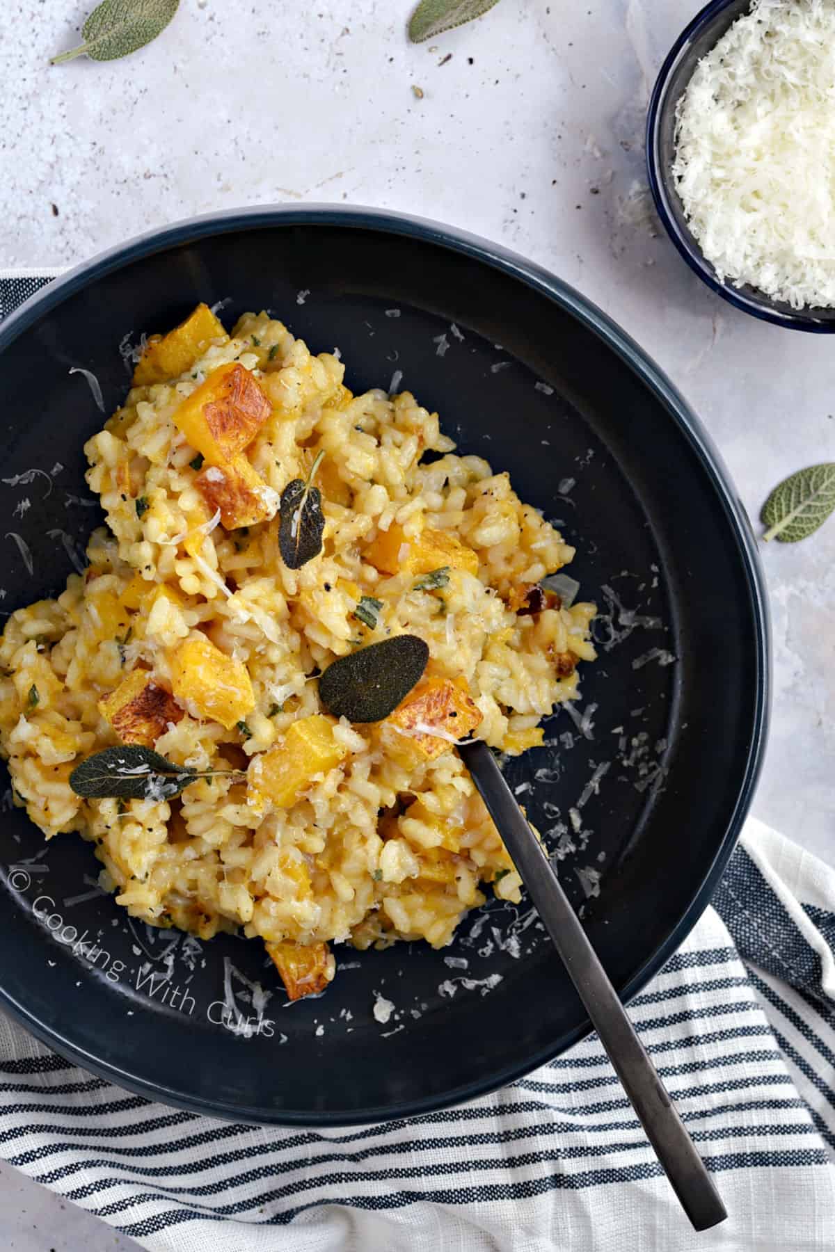 Looking down on a blue bowl with risotto, cubes of roasted butternut squash, crispy sage leaves and grate parmesan.