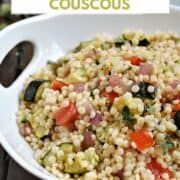 A serving bowl filled with Israeli couscous tossed with roasted red pepper, zucchini, and red onion with title graphic across the top.