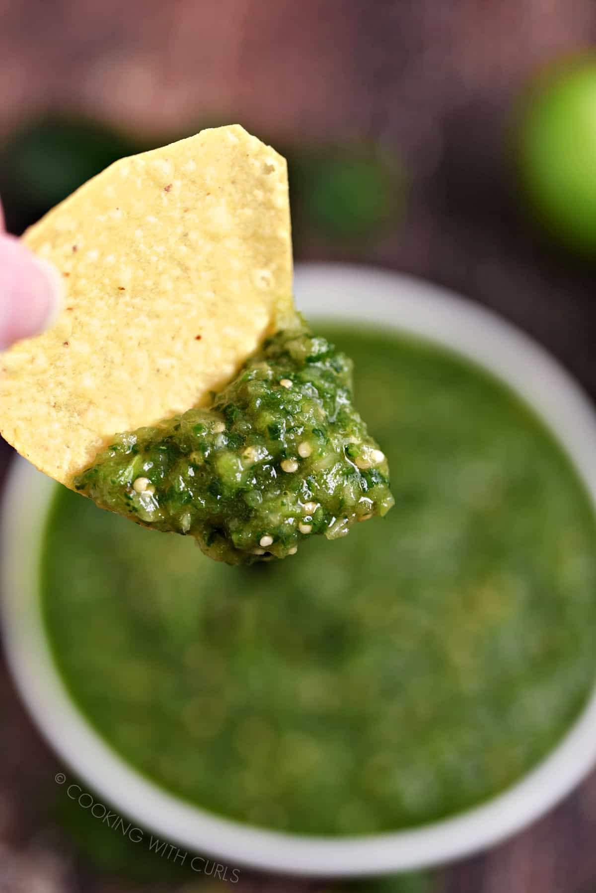 Salsa Verde on a tortilla chip above the bowl of salsa. 