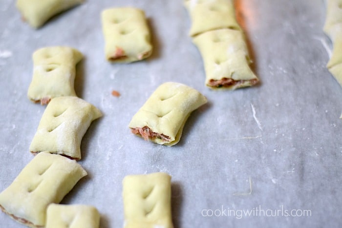 Ten Puff Pastry Sausage Rolls pierced with vent holes sitting on a marble board. 