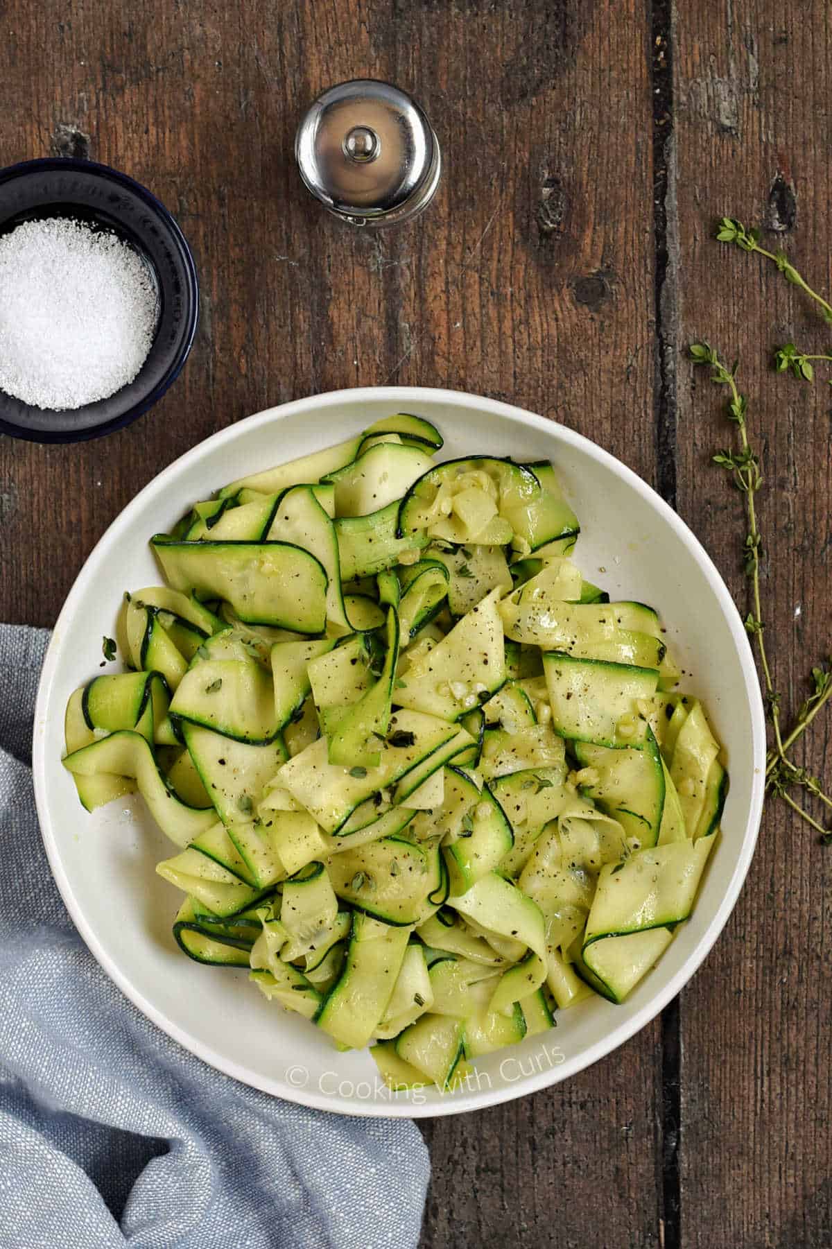 Looking down on a bowl of sauteed zucchini ribbons topped with black pepper and fresh thyme leaves.