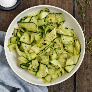 Looking down on a bowl of sauteed zucchini ribbons topped with black pepper and fresh thyme leaves.