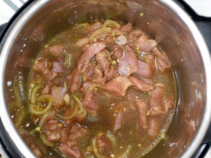 Seasoned chicken pieces added to the stock, soy sauce, onions and garlic inside the metal liner of a pressure cooker 