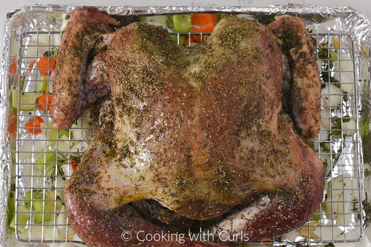 Seasoned turkey on a wire rack above chopped, fresh vegetables on a baking sheet. 