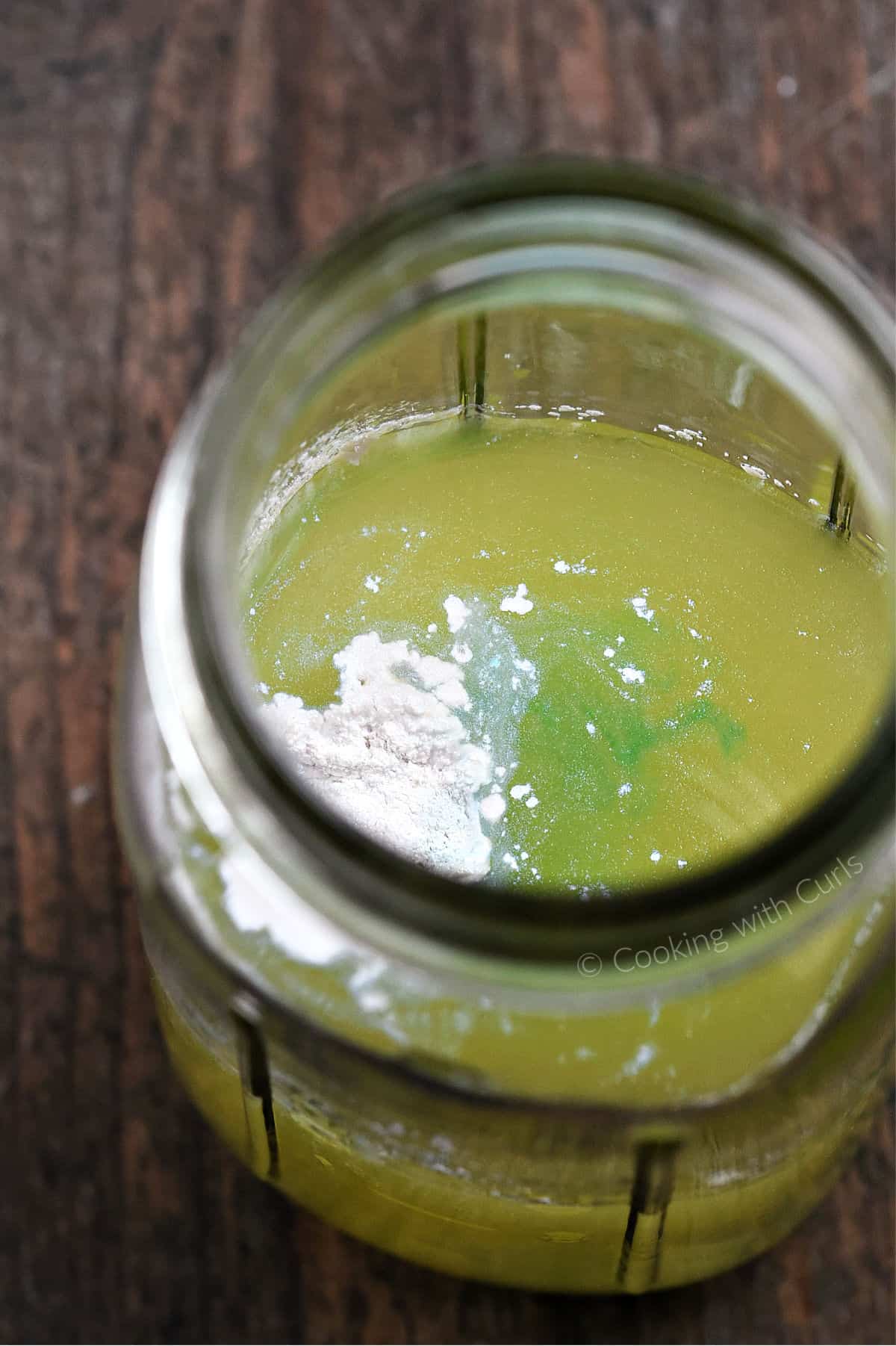 Shimmer powder and a drop of teal coloring in a pineapple juice and alcohol mixture in a cocktail shaker. 