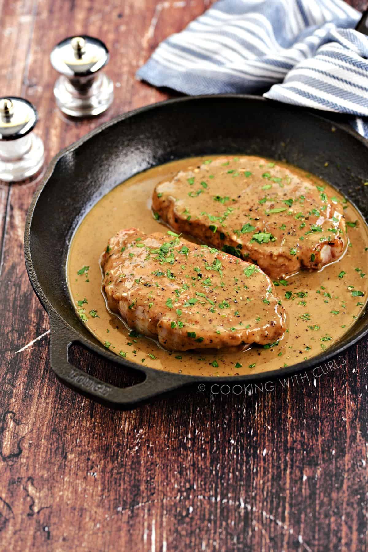Two pork chops smothered with brown pan gravy in a cast iron skillet.