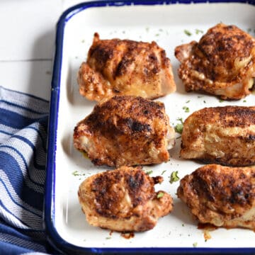 Close up image of six crispy chicken thighs on a white platter.