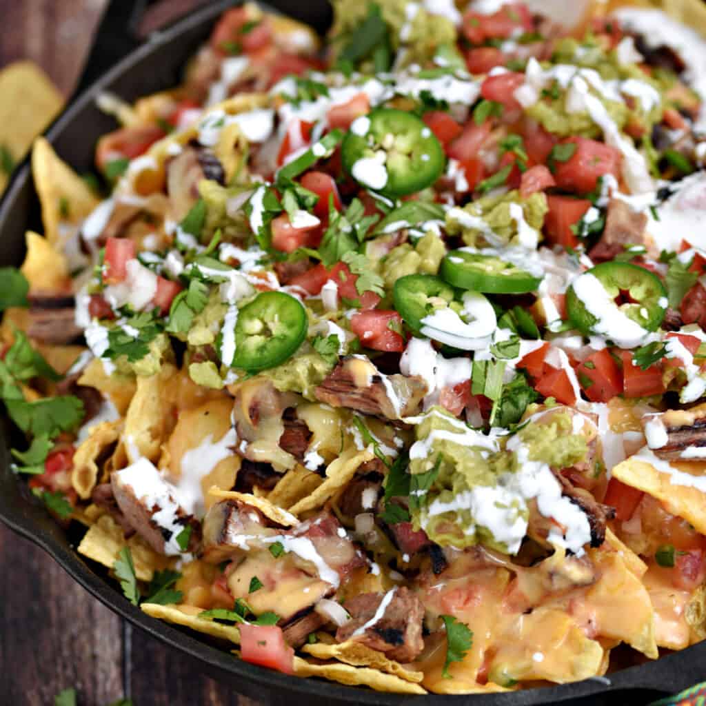 Tortilla chips topped melted cheese, steak, jalapeno slices, cilantro, and drizzled with crema in a cast iron skillet.