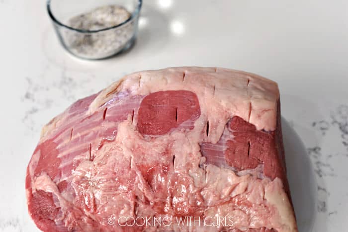Slits cut into roast with a glass bowl of salt and pepper in the background. 