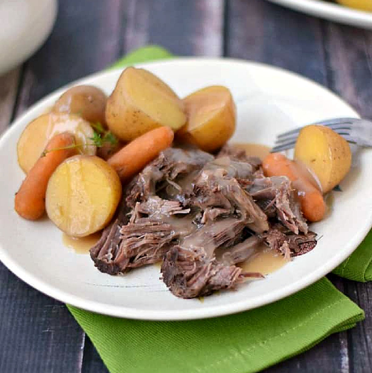 Pot roast, baby carrots, and potatoes on a plate covered with gravy.