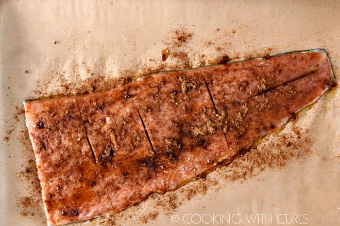 Spices sprinkled over salmon filet on a parchment lined baking sheet. 