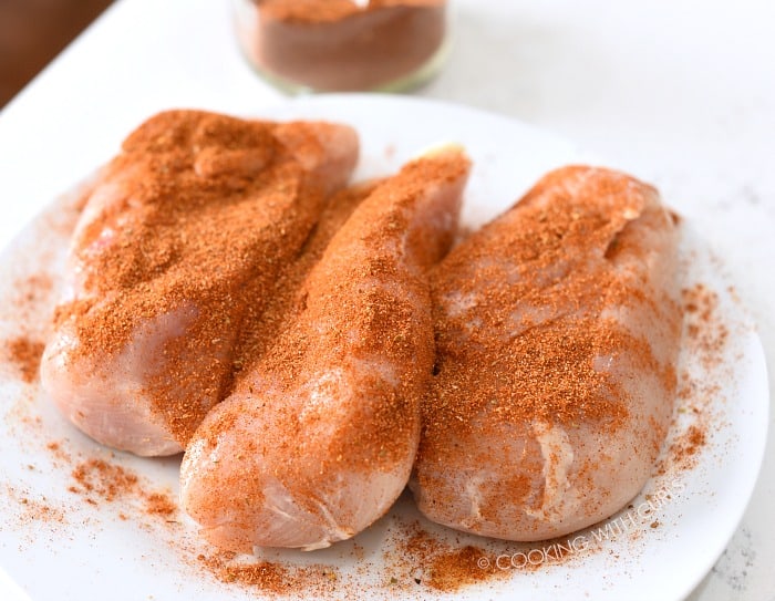 Taco seasoning sprinkled over the chicken breasts on a white plate.