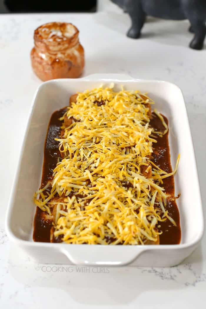 Rolled chicken enchiladas in a baking dish topped with grated cheese.