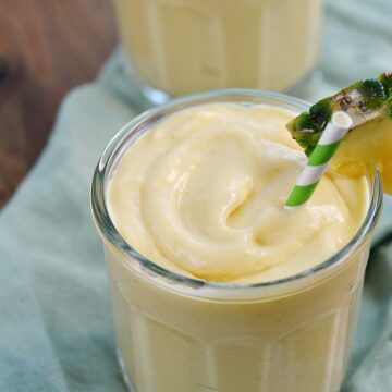 Two glasses filled with Mango Pina Colada Smoothie garnished with a pineapple wedge and green and white striped straw