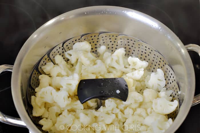 Steamed cauliflower in a metal steamer inside a large pot. 