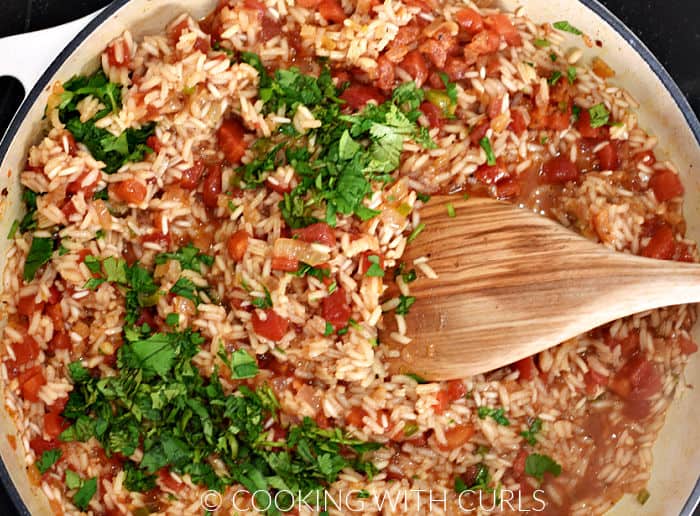 Stirring cilantro into the Mexican rice with a wooden spoon. 