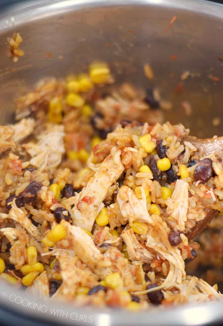 Stirring the Instant Pot Chicken Taco Bowls together with a large wooden spoon.